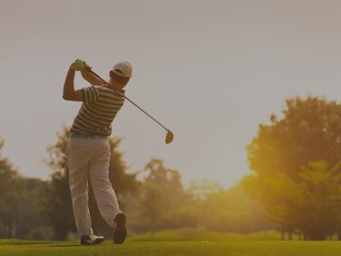 Tourisme Montérégie | Homme de dos avec bâton de golf terminant sa swing au couché du soleil