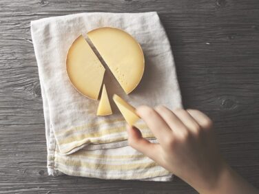 Tourisme Montérégie | Vue en plongée d'une main prenant un morceau d'une meule de fromage